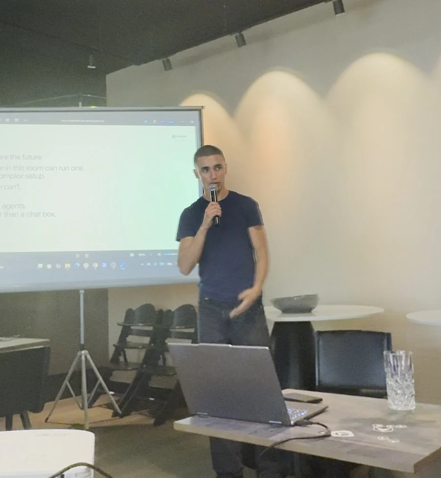 Jayden Bruck speaking into a microphone at Cursor Build Day in Frankfurt, with his Ola slide projected on the screen behind him.